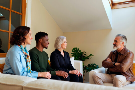 Diverse group of middle aged Caucasian woman, Black man, senior Caucasian woman and senior Caucasian man sitting together on sofa, engaging in conversation, smiling, facing each other