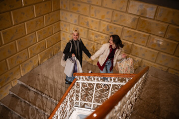 Happy young women friends holding hands carrying shopping bags