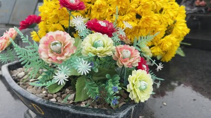 Close-up of colorful artificial flowers in a pot on a wet tombstone in a cemetery - Powered by Adobe