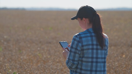 A young woman is using her smartphone while standing in an expansive agricultural field