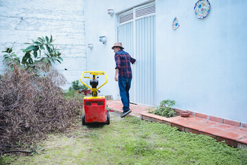 Man wearing a hat and plaid shirt, walking towards a door in a backyard, having just used or...