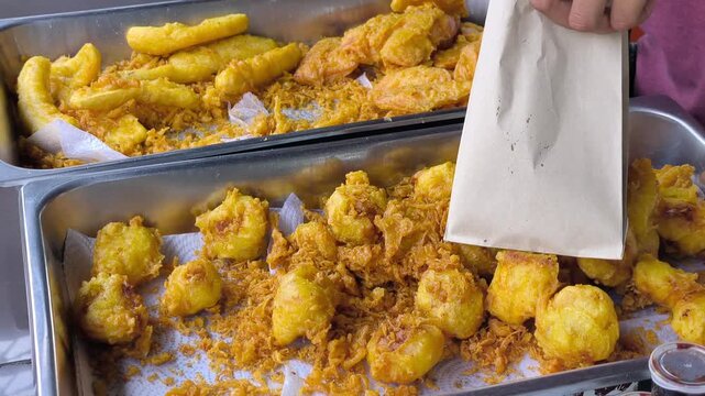 Fresh cempedak fruit is coated in turmeric-infused batter and deep-fried in hot cooking oil. This popular Malaysian street food snack is often enjoyed for its sweet, crispy flavor.