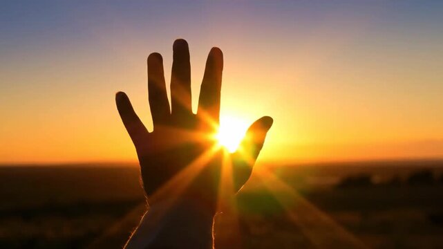 The image shows a man standing with his back to the viewer and looking towards the sunset. He raises his hand, and his palm is facing the sun, as if he is trying to protect himself from the bright lig