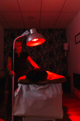 Woman receiving back therapy with a heat lamp, a physiotherapist assisting. Focusing on pain relief and muscle relaxation