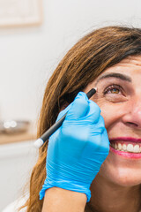 Professional drawing lines on mature woman's face, preparing for cosmetic injections to reduce wrinkles around her eye