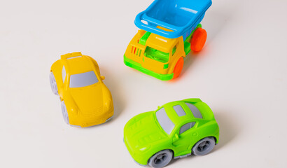 Obraz premium Brightly colored toy cars, including a green sports car, a yellow car, and a blue dump truck, are placed together on a clean surface, inviting kids to engage in imaginative play indoors.