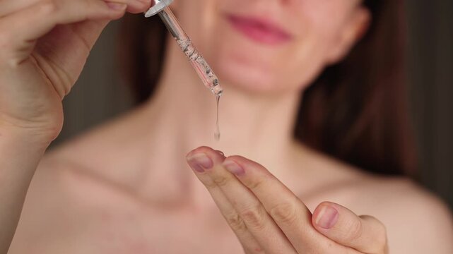 Close-up of a woman using a dropper as transparent liquid drops slowly fall onto her fingers, representing skincare or serum application. 