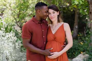 Interracial couple embracing in nature during pregnancy celebration