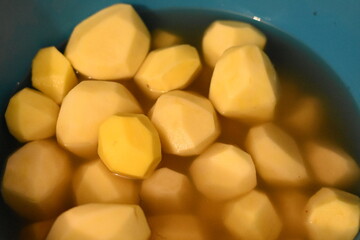Peeled potatoes in a blue bowl with water, close-up.