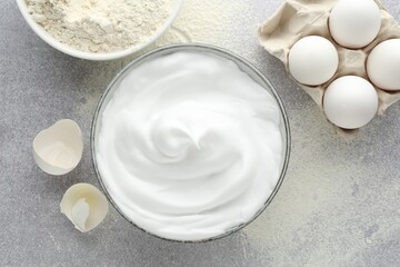 Beating whites in bowl, eggs, eggshell and flour on grey textured table, flat lay