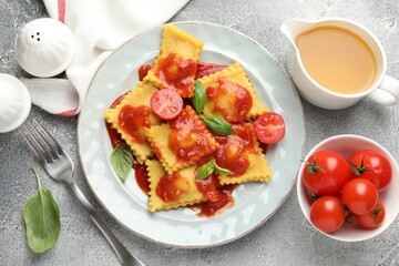 Delicious ravioli with tomato sauce and basil served on grey table, flat lay