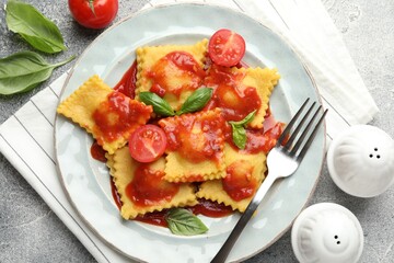 Delicious ravioli with tomato sauce and basil served on grey table, flat lay