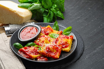 Delicious ravioli with tomato sauce, cheese, grater and basil on grey table, closeup. Space for text
