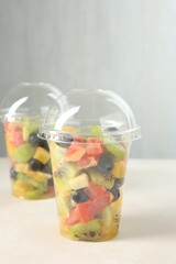 Tasty fruit salad in plastic cups on beige table, closeup