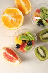 Tasty fruit salad in plastic cups and ingredients on beige table, flat lay. Healthy snack