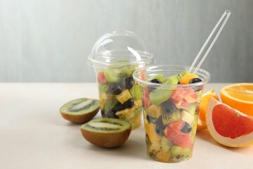 Healthy snack. Tasty fruit salad in plastic cups and ingredients on beige table, closeup. Space for text