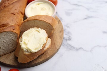 Cut baguette with butter on white marble table, closeup. Space for text