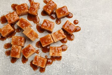 Tasty candies with salt and caramel sauce on grey textured table, flat lay. Space for text