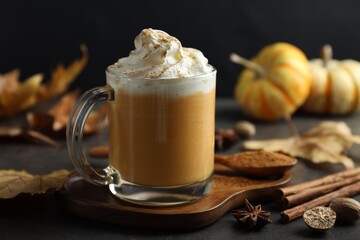 Tasty pumpkin latte with whipped cream in glass cup, spices and autumn decor on grey table, closeup
