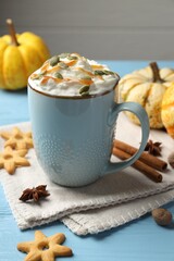 Tasty pumpkin latte with whipped cream in cup, spices and cookies on light blue wooden table, closeup