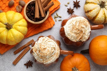 Tasty pumpkin latte with whipped cream in cups, spices and ingredients on light grey table, flat lay