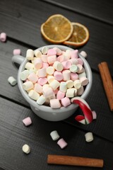 Tasty hot cocoa with marshmallows, candy cane, cinnamon and dried orange slices on wooden table, closeup. Christmas season