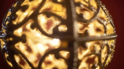 Ornate gold lamp illuminated, warm light glowing through filigree, on red backdrop, for mood, background, decoration - Powered by Adobe