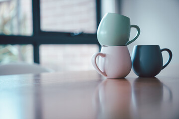 Colorful  stackable ceramic mugs  on wooden table in soft minimal style.