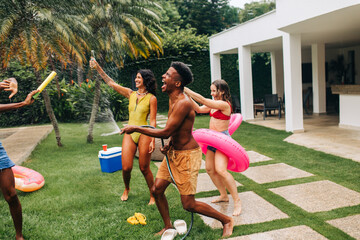 Obraz premium Friends celebrate backyard water fight and pool party