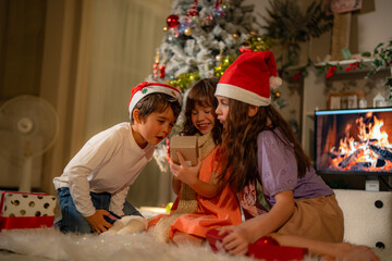 Three children celebrate Christmas at home, exchanging holiday gifts in front of a decorated tree. Smiling and joyful, they enjoy the warmth and excitement of the festive season.