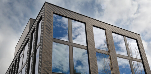 Modern building exterior, large reflective windows shows blue sky and clouds. Minimalist urban style real estate, residential apartment, office building architecture