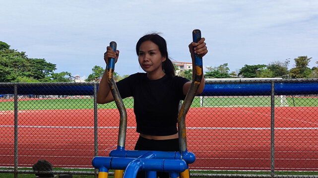 Woman Exercising Outdoors: A woman engages in a cardio workout on an elliptical machine outdoors, focusing on physical well-being and health in a vibrant environment.