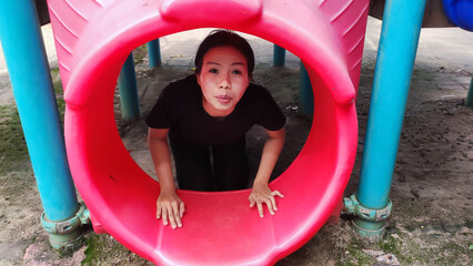 Playground Discovery: A moment of playful exploration as a person peers through the vibrant red tunnel of a playground, inviting a sense of childlike wonder.