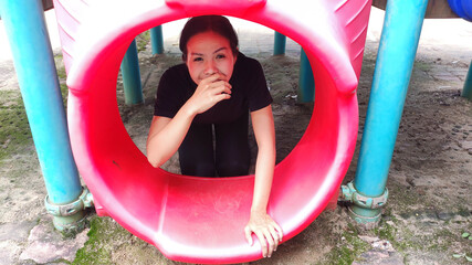 Joyful Play: A young female joyfully peeks through the brightly colored playground equipment, her expression radiating happiness and youthful energy.