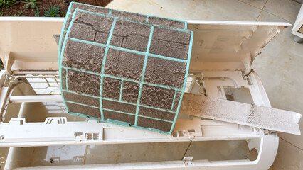Close-up of a heavily dust-covered air conditioner filter with turquoise frame showing accumulated...