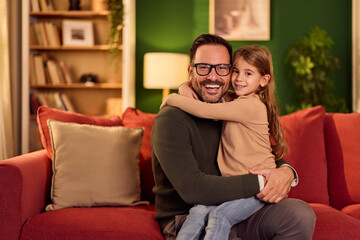 Obraz premium Warm Family Moment: Father And Daughter Embrace On Cozy Red Couch In Living Room