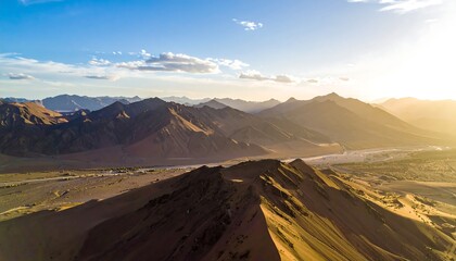Aerial shot of majestic golden mountains under a blue sky with clouds, glowing in sunlight