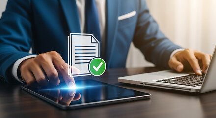 Businessman reviews digital documents on a tablet with approval icon, while working on a laptop, showcasing modern business practices