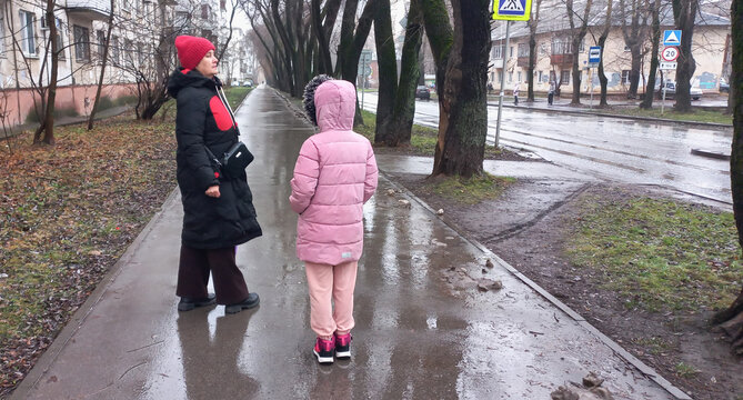Woman talking to child while walking on rainy street in autumn - Powered by Adobe