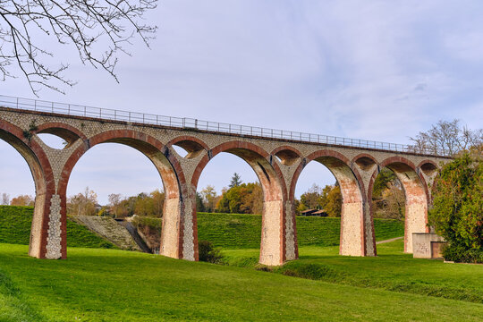 Historic brick railway viaduct with stone arches crossing a green valley near a small reservoir in Boulogne-sur-Gesse, symbolizing French industrial heritage and civil engineering 