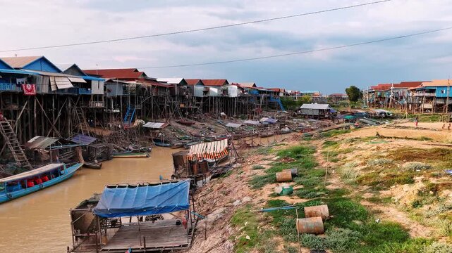 Traditional houses on stilts and fishing boats lining the muddy riverbank of kampong phluk, a floating village on tonle sap lake.
