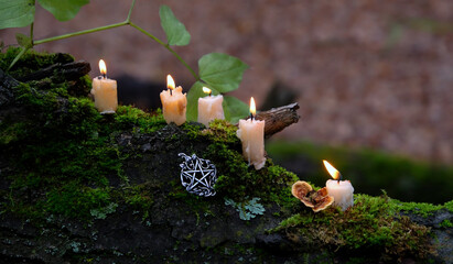 burning wax candles and witch pentacle amulet close up on mossy trunk, abstract natural dark forest background. magical candles for witchcraft, esoteric ritual. fairytale, mystery atmosphere