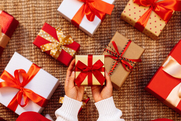 Obraz premium Small present with red ribbon and bow in hands above the gift boxes on the floor.