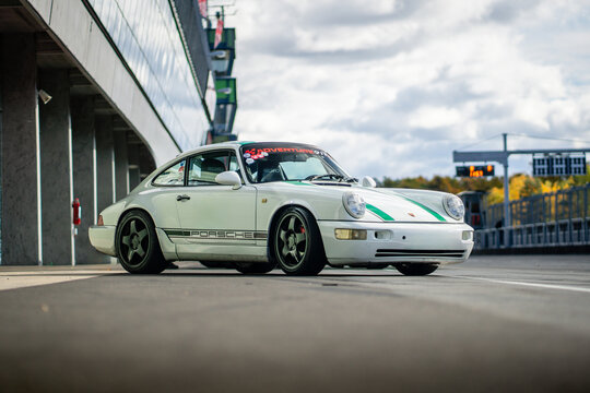Brno, Czech Republic - October 10, 2025: Sports car Porsche 911 with the designation 964 Carrera from 1991 in white with green stripes stands in the pits on the racing circuit.