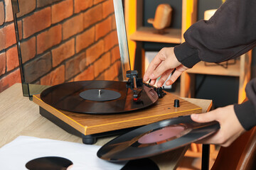 Woman turning record player with vinyl disk on at home, closeup