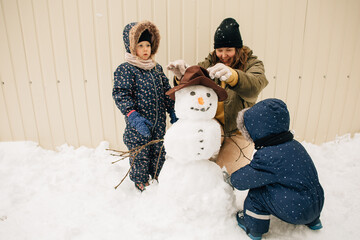 Family building snowman in winter yard with children