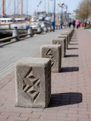 Fototapeta premium Stone bollards line a marina pathway with boats in the background.
