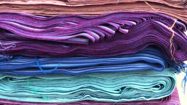 Close-up view of layered fabric rolls stacked neatly in various colors and textures. Ideal for themes related to textiles, fabric markets, garment production, clothing materials, fashion, and craft in
