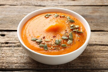 Tasty pumpkin cream soup with seeds served on wooden table, closeup