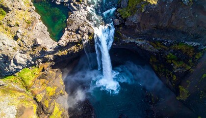 Overhead view of a waterfall plunging into a pool surrounded by mossy rocks and rugged terrain